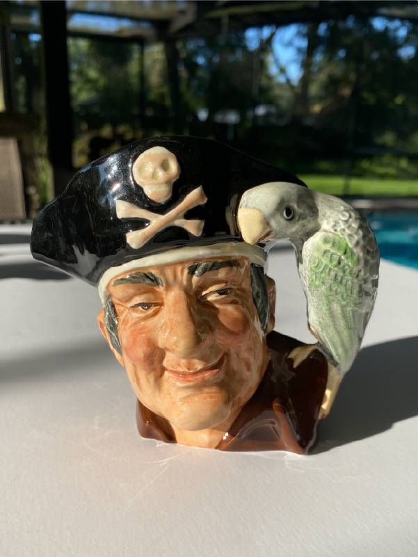 Ceramic mug shaped like a pirate's head wearing a black hat with a skull and crossbones, featuring a green and gray parrot perched on the handle.
